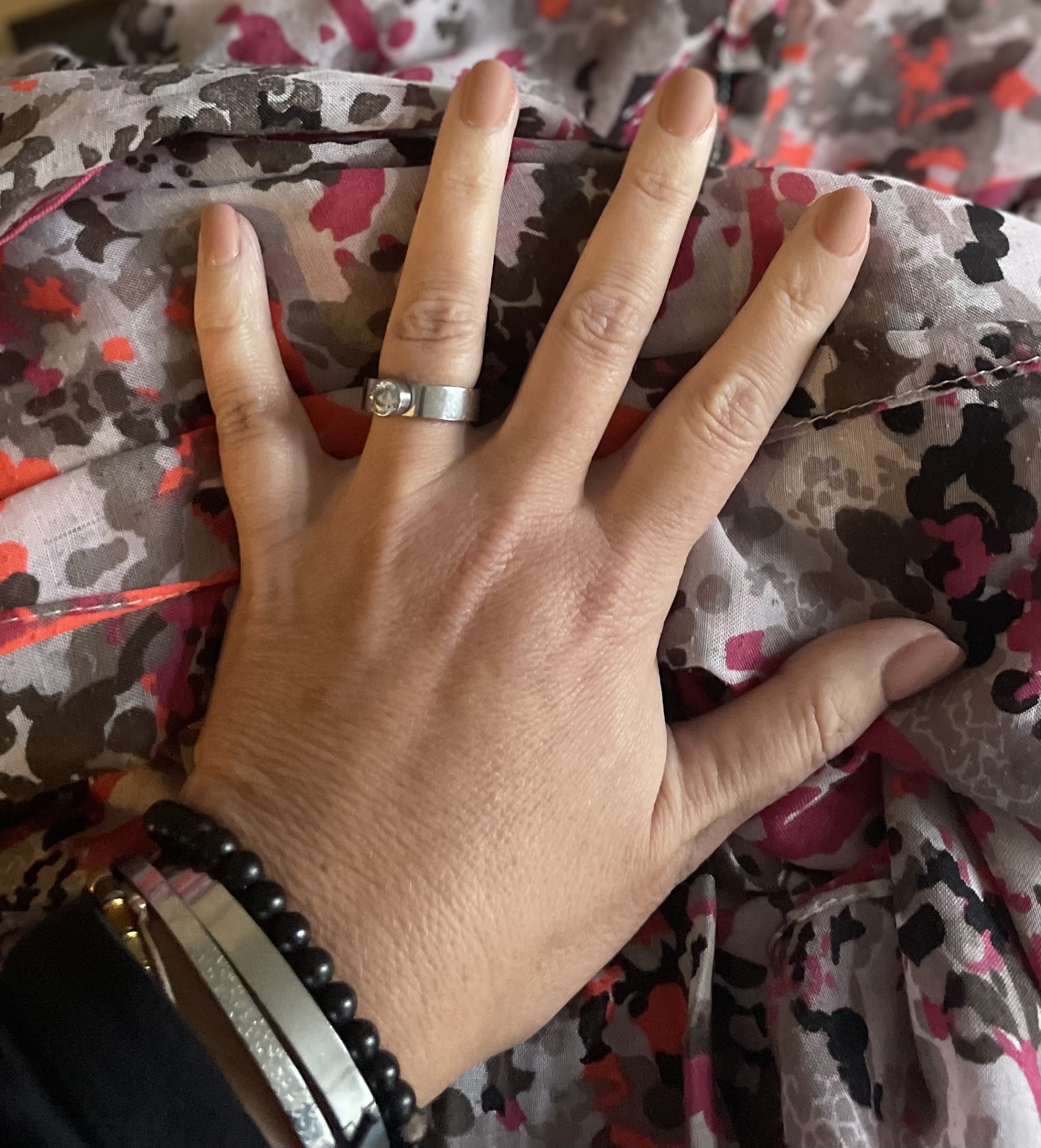 Hand met naturelkleurige nagels op een gebloemde blouse
